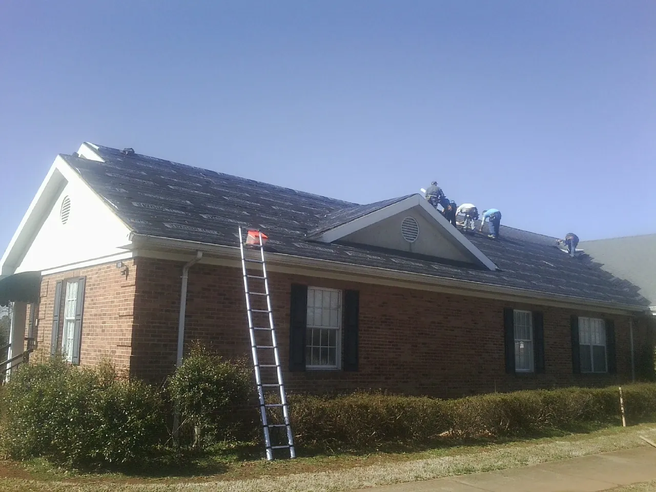Crew tearing shingles off a brick ranch roof with a ladder set — Metal Roof Repair work by our crew in Upperville