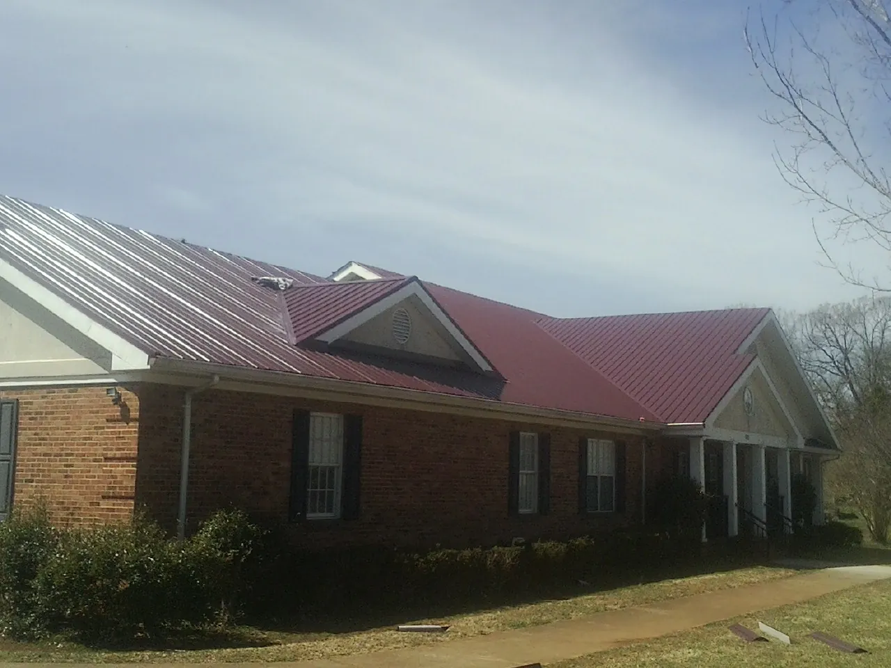 Red metal roof with gabled entries on a long brick building, from a Hail Damage Roof Repair job in Upperville