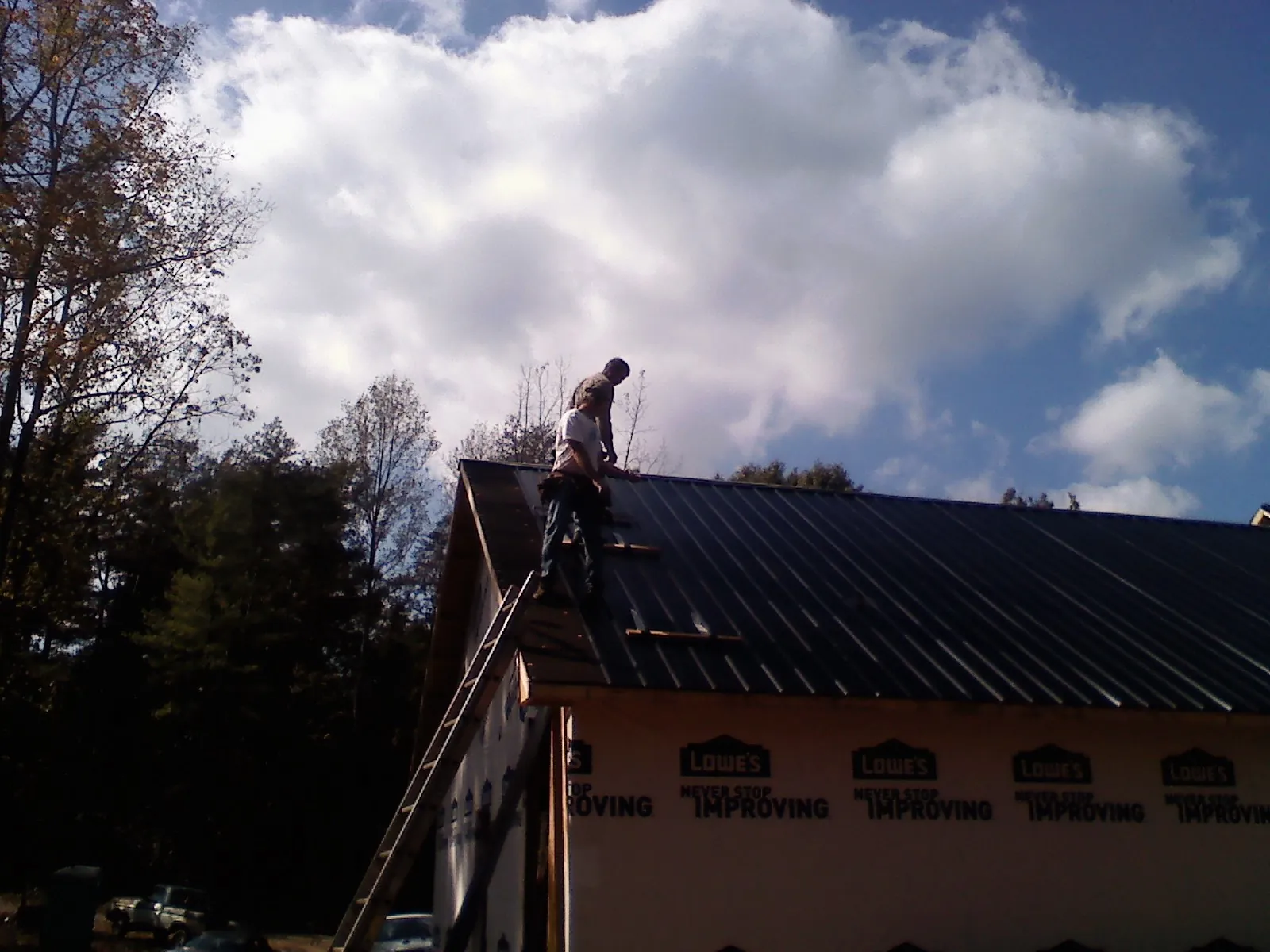 Roofer fastening dark metal panels high against a cloudy sky, from a Roof Inspection job in Upperville