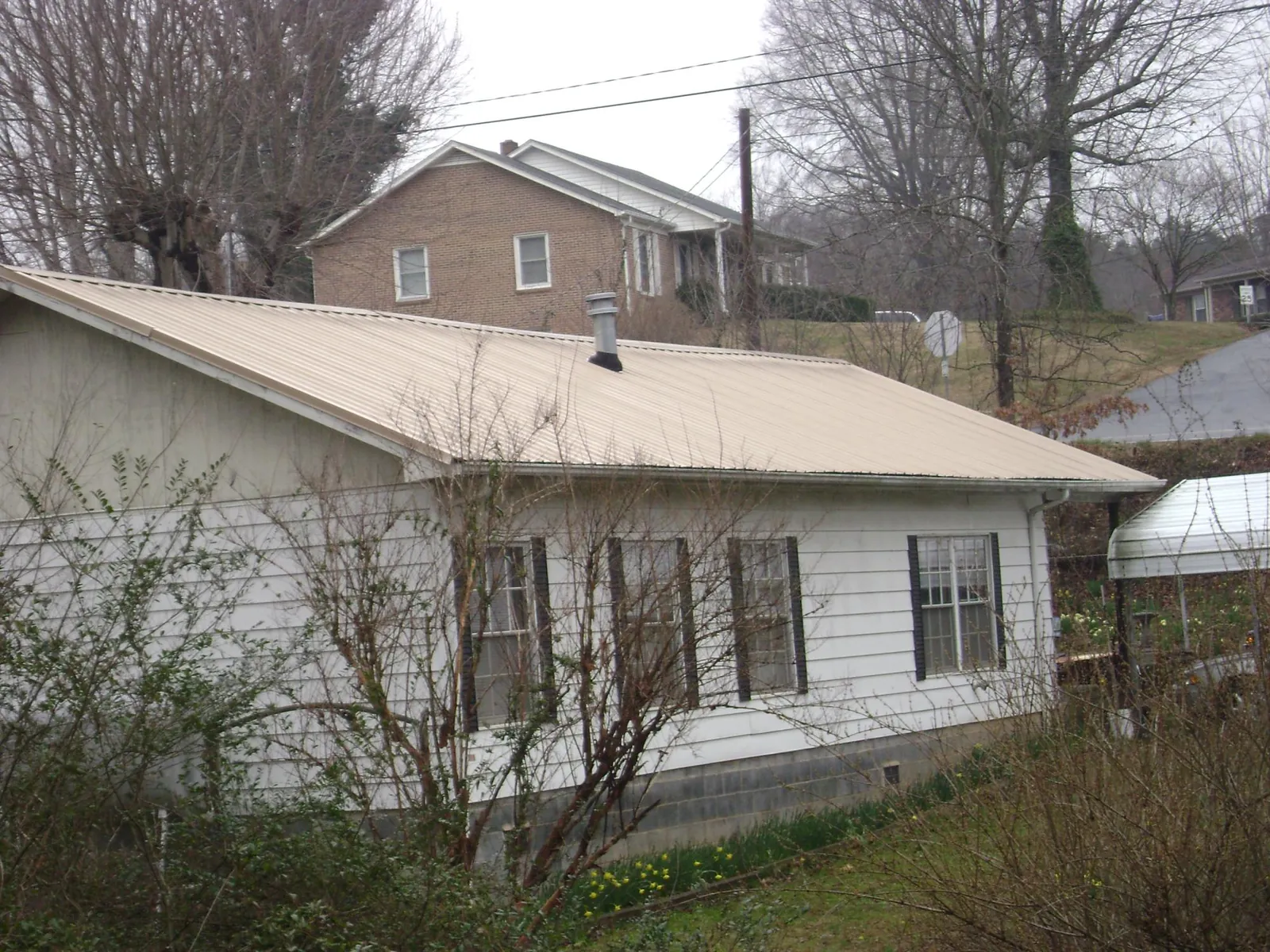 Tan metal roof on a white sided house set into a hillside — Commercial Roofing by Roofing Brothers in Upperville